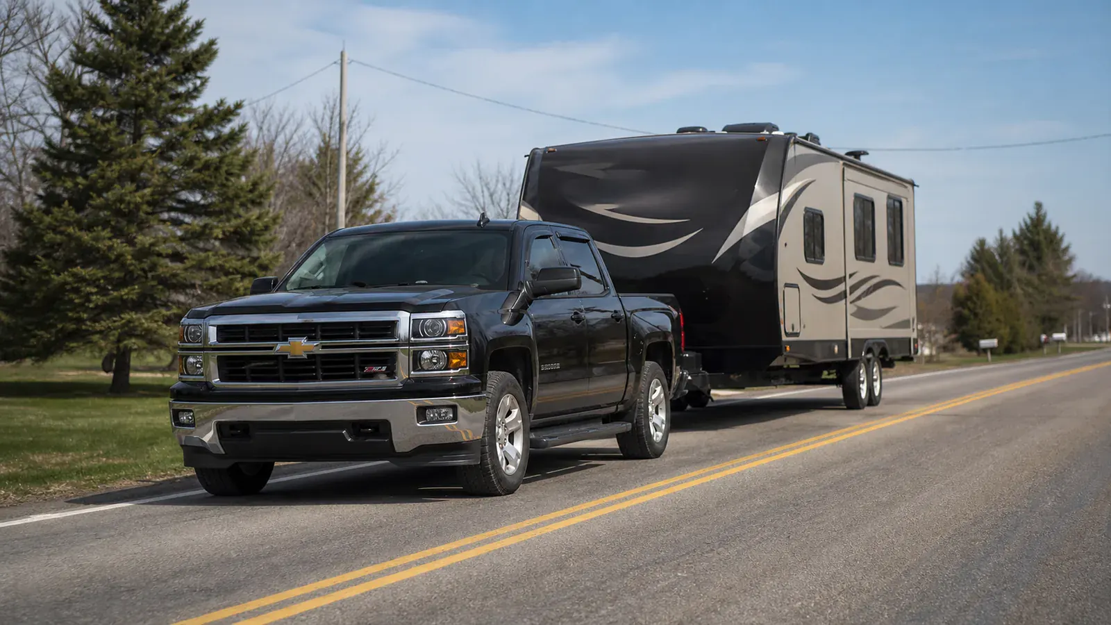 Black pickup truck hauling an RV on a Quebec road.
